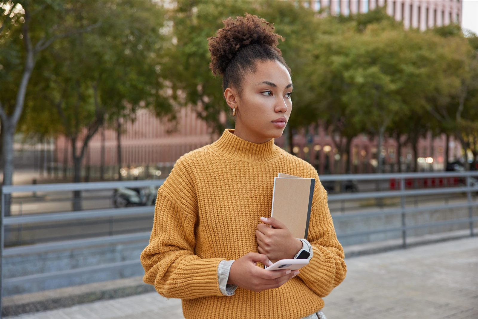 Estudante segurando cadernos e celular em frente ao campus